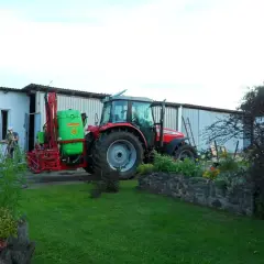 Czerwony traktor z opryskiwaczem czeka na deszcz. Rolnik przygotowuje sprzęt, by zdążyć przed ulewą.