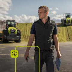 Rolnik z telefonem w ręku, symbolizujący rolnictwo 4.0, na tle nowoczesnych maszyn rolniczych i pól.