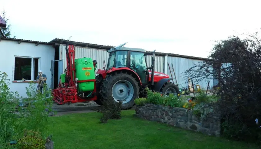 Czerwony traktor z opryskiwaczem czeka na deszcz. Rolnik przygotowuje sprzęt, by zdążyć przed ulewą.